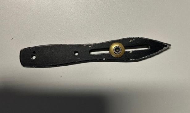 Ein schwarzes Wurfmesser mit einem goldenen Knopf liegt auf einem hellen Untergrund.