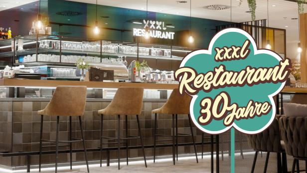 Die modern eingerichtete Bar eines XXXLutz Restaurants ist mit einem großen Jubiläumslogo „30 Jahre“ dekoriert.