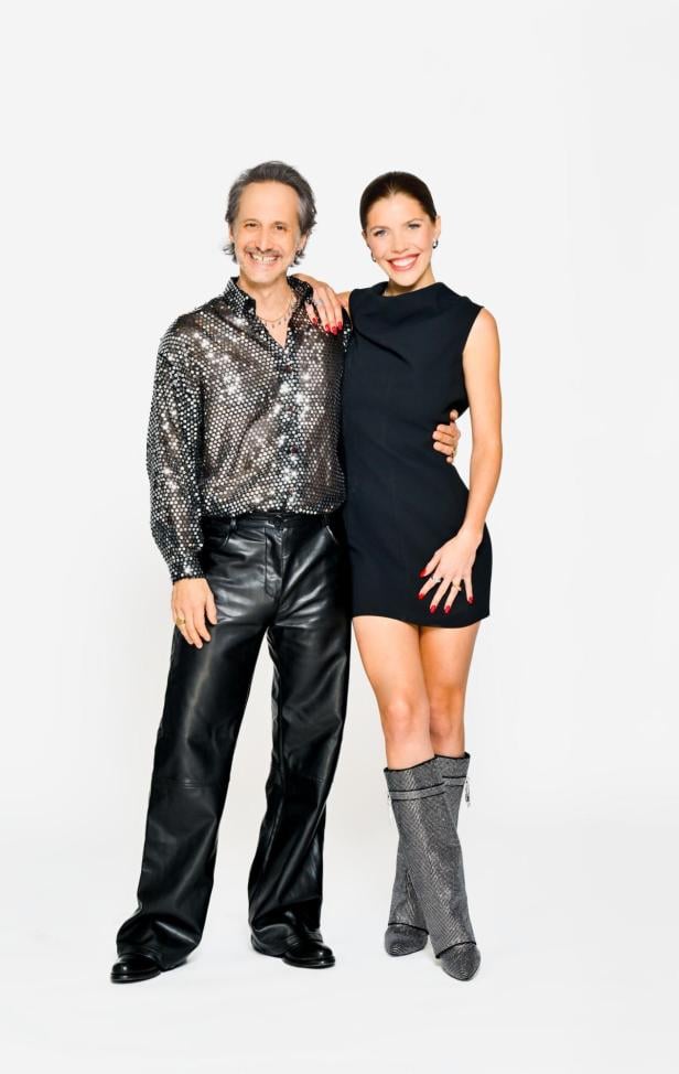 Ein Mann in Glitzerhemd und Lederhose steht neben einer Frau im schwarzen Kleid und silbernen Stiefeln.