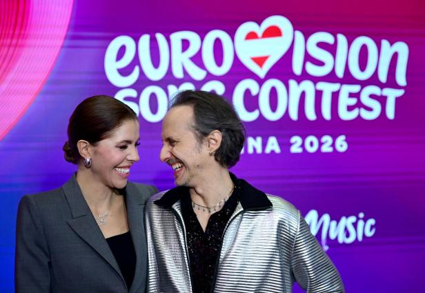 Zwei lachende Menschen stehen eng beieinander vor einem Eurovision Song Contest Wien 2026 Schriftzug.