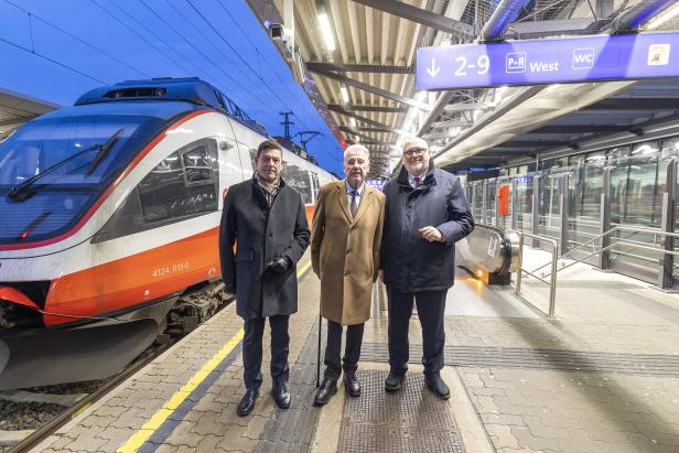 Drei Männer stehen auf einem Bahnsteig vor einem Zug.