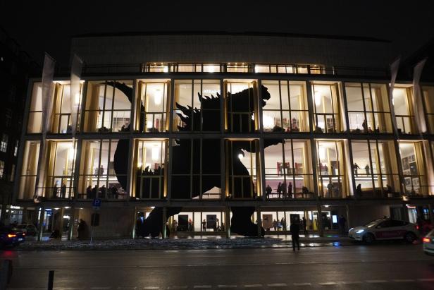 Großes Gebäude mit beleuchteten Fenstern, in denen eine schwarze Godzilla-Silhouette sichtbar ist.