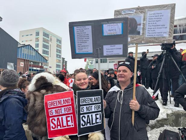 Menschen demonstrieren mit Schildern, auf denen steht „Greenland is not for sale!“, in einer winterlichen Stadtumgebung.