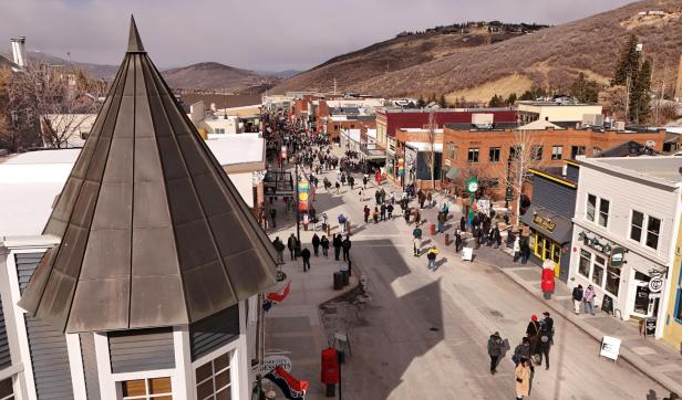 Viele Menschen spazieren auf einer belebten Einkaufsstraße mit Geschäften, umgeben von Hügeln und Häusern.