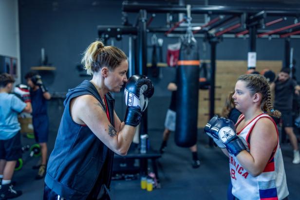 Zwei Personen mit Boxhandschuhen stehen sich in einem Fitnessstudio gegenüber und trainieren konzentriert.