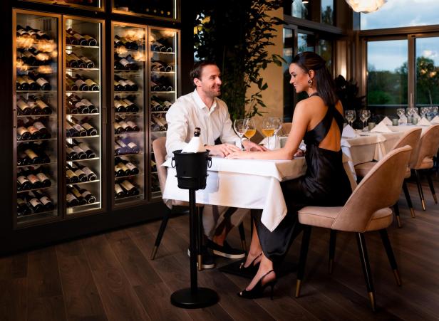 Paar genießt romantisches Abendessen mit Wein in elegantem Restaurant vor Weinschränken.