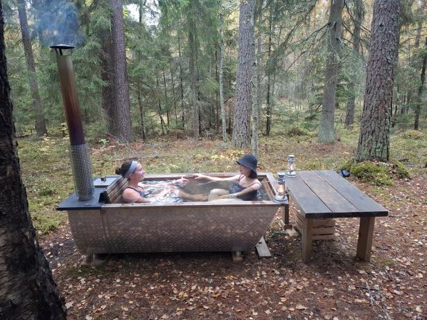 Zwei Frauen entspannen in einem mit Holz beheizten Badezuber im Wald.