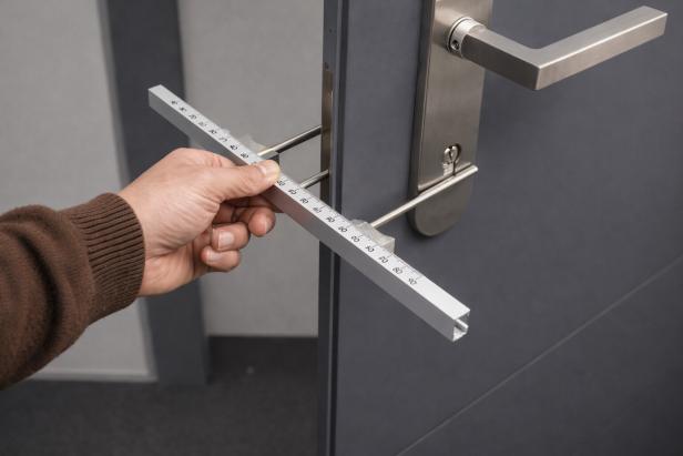 Hand misst mit Lineal die Dicke einer Tür mit moderner Edelstahlgarnitur aus.