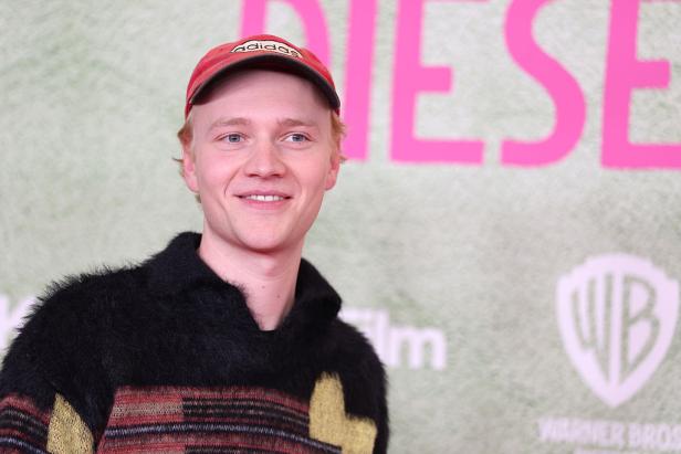 Bruno Alexander lächelt bei einer Filmpremiere vor einem Hintergrund mit Warner Bros.-Logo und großem Schriftzug.