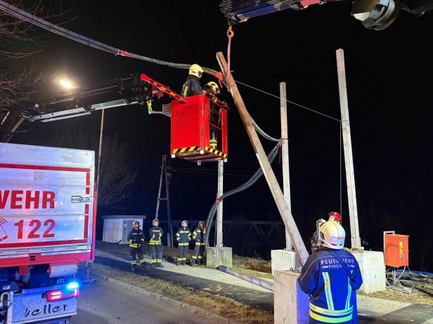 Feuerwehrleute arbeiten nachts mit einem Kran an einer beschädigten Stromleitung und sichern den Bereich.