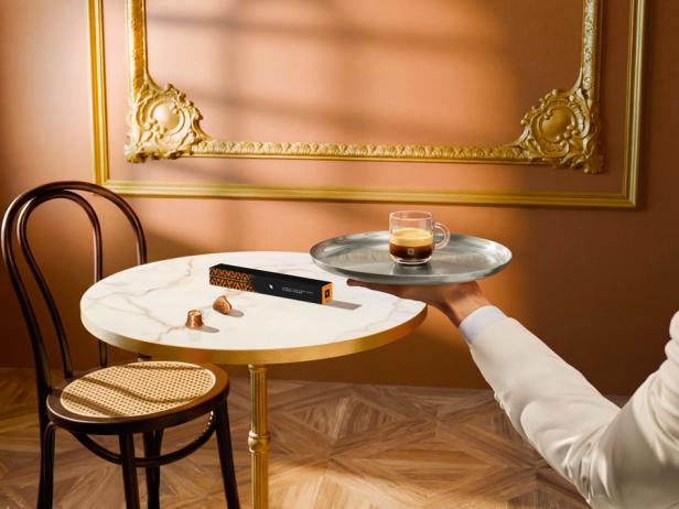 Ein Mann in einem weißen Anzug hält ein Tablett mit einer Kaffeetasse.