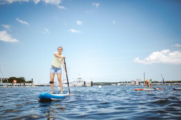 Eine Frau steht auf einem Paddleboard auf dem Wasser und hält ein Paddel.