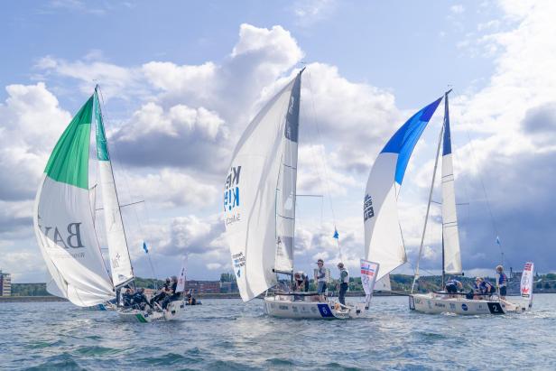 Mehrere Segelboote mit farbigen Segeln nehmen an einer Regatta auf dem Wasser teil.