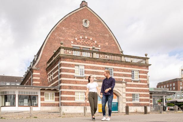 Zwei Menschen spazieren lachend vor dem historischen Backsteingebäude des Schifffahrtsmuseums in Kiel.