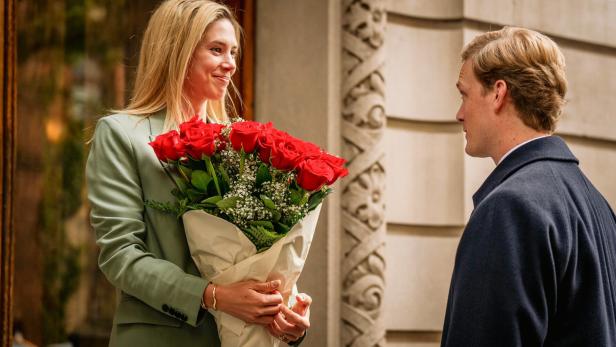 Eine Szene aus "Máxima": Máxima (Delfina Chaves) hält einen großen Strauß roter Rosen und lächelt Willem-Alexander (Martijn Lakemeier) an, der ihr gegenübersteht.
