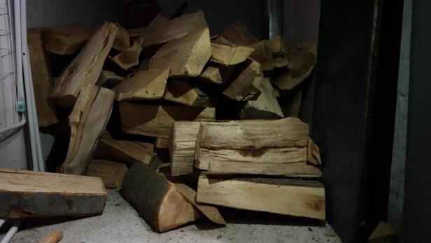 Ein Stapel gespaltenes Brennholz liegt auf einem Boden in einem dunklen Raum.