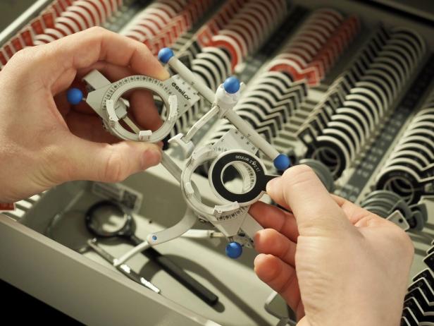 Eine Hand justiert eine Messbrille vor einem Kasten mit Linsen.