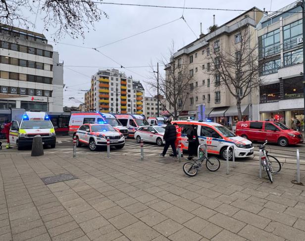 Mehrere Einsatzfahrzeuge mit Blaulicht und Rettungskräfte stehen auf einer belebten Straße in einer Stadt.