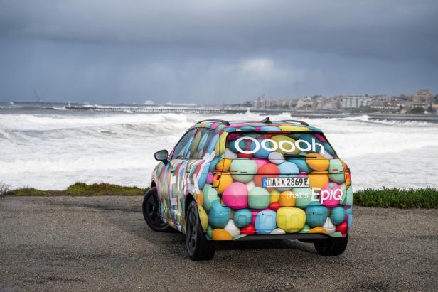 Škoda Epiq mit bunter Camouflage-Folie steht am Meer vor stürmischer Küste.