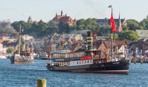 Der historische Salondampfer Alexandra fährt während eines maritimen Festes durch den Flensburger Hafen, im Hintergrund die Altstadt mit markanten Gebäuden.