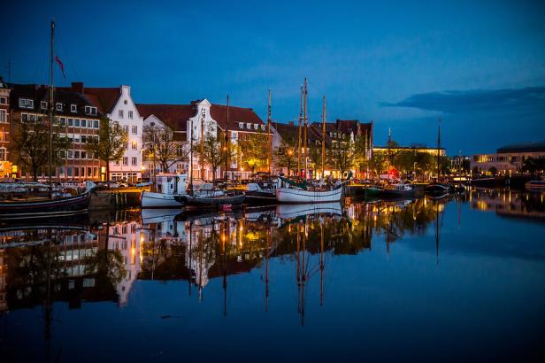 Am Abend spiegeln sich Häuser und Boote im ruhigen Wasser eines Kanals.