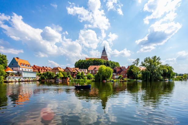 Blick auf die Altstadt von Mölln mit Fachwerkhäusern, Kirche und See, während ein Boot auf dem Wasser fährt.