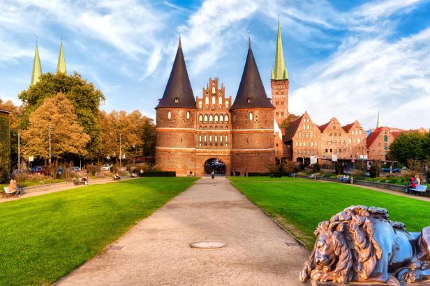 Das Holstentor in Lübeck mit seinen markanten Türmen und der Backsteinarchitektur, flankiert von Grünflächen und historischen Gebäuden, symbolisiert das UNESCO-Welterbe der Hansestadt.