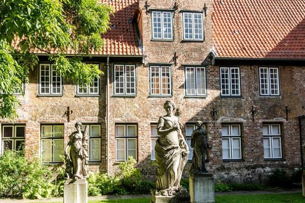Drei historische Statuen stehen im sonnigen Innenhof vor einer Backsteinfassade mit roten Dachziegeln in der Lübecker Altstadt.