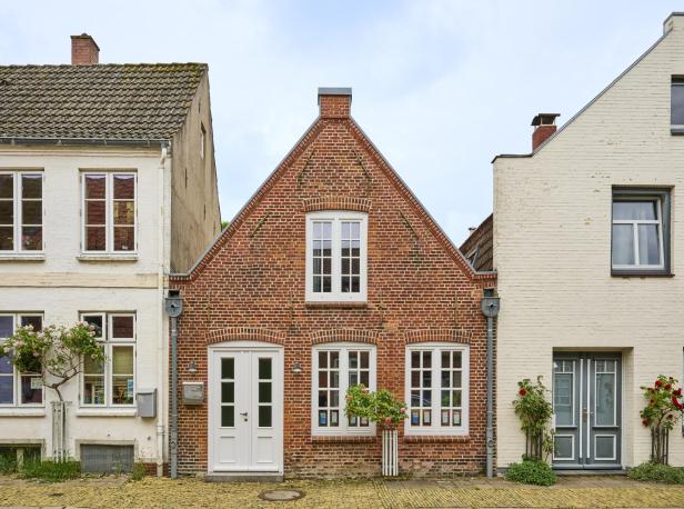 Typisches Treppengiebelhaus aus rotem Backstein in Friedrichstadt, eingerahmt von weißen Nachbarhäusern und kleinen Rosenbüschen.