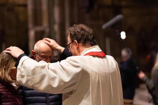 Ein Geistlicher legt zwei Personen in einer Kirche die Hände segnend auf den Kopf.