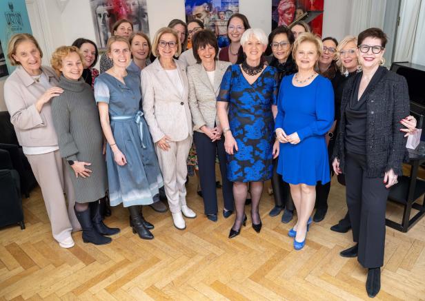 Eine Gruppe von Frauen unterschiedlichen Alters steht lächelnd in eleganter Kleidung in einem hellen Raum zusammen.