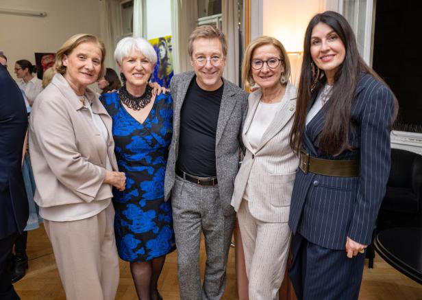 Fünf Personen stehen eng beieinander und lächeln in eleganter Kleidung in einem hellen Raum.