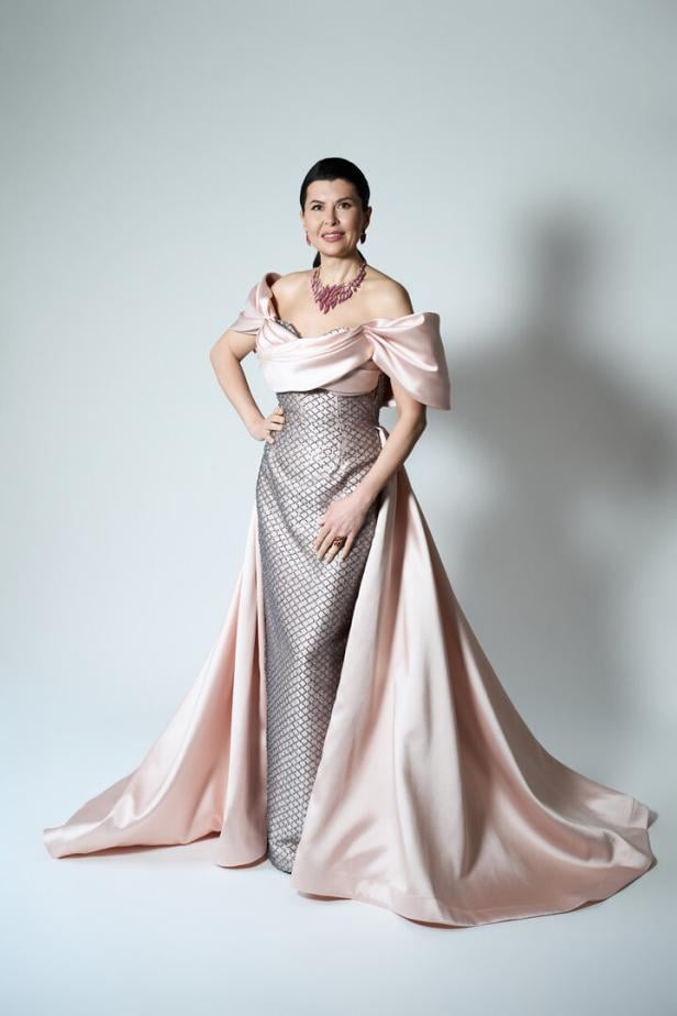 Frau mit elegantem, bodenlangem Kleid in Rosa und Silber, schulterfrei, mit auffälliger Halskette.