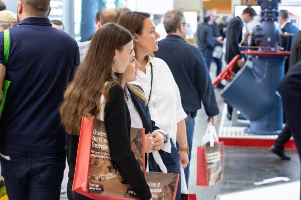 Besucherinnen mit Messetaschen betrachten Ausstellungsstücke auf einer Fachmesse für Energie und Bau.