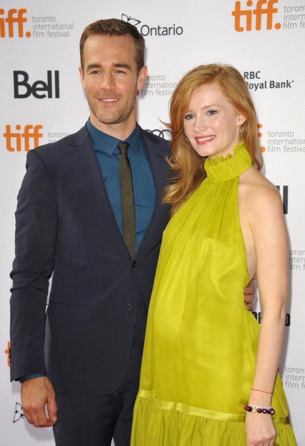 Ein Mann im Anzug und eine Frau im grünen Kleid lächeln gemeinsam vor einer Sponsorenwand.