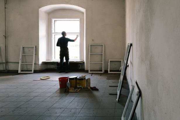 labour worker paints a window frame in an old empty house