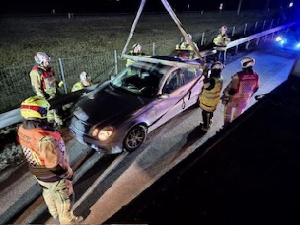 Feuerwehrleute bergen nachts ein beschädigtes Auto mit einem Kran auf der Autobahn.
