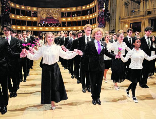 Mehrere junge Paare in festlicher Kleidung tanzen in einem prunkvollen Saal und halten Blumen in den Händen.