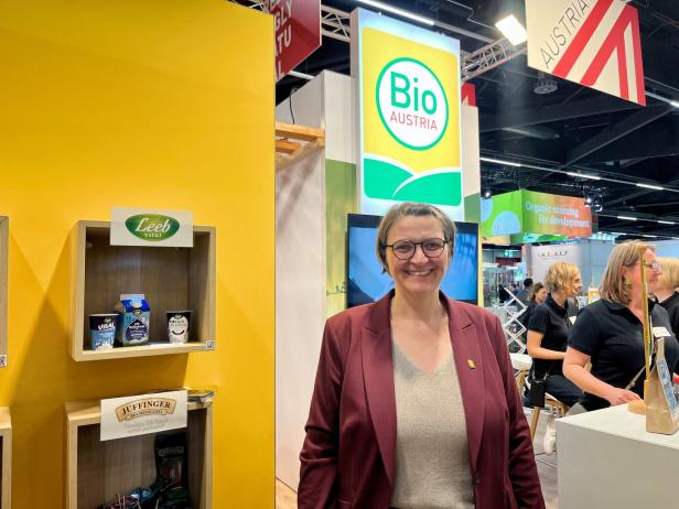 Ein Frau steht lächelnd an einem Messe-Stand mit einem leuchtenden Schild im Hintergrund mit der Aufschrift "Bio Austria".