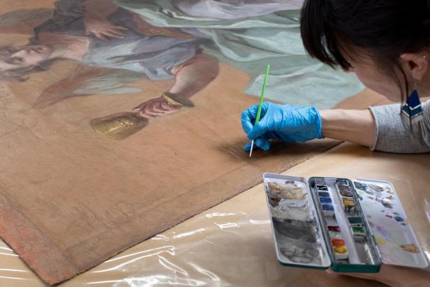 Eine Aufnahme von einer Frau die einen Pinsel hält und damit ein Bild restauriert.
