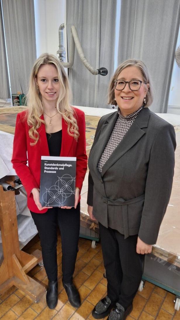 Zwei Frauen stehen nebeneinander, eine hält die Broschüre.