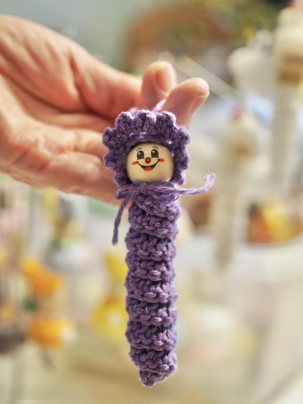 Ein Häkel-Wurm aus violettem Garn mit einer Perle samt aufgezeichnetem Gesicht als Kopf.