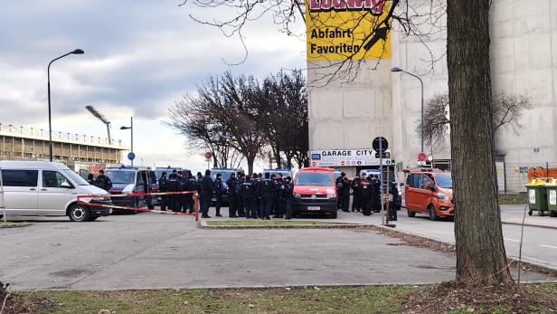 Viele Polizisten stehen vor mehreren Einsatzfahrzeugen und einem abgesperrten Bereich nahe einer Tiefgarageneinfahrt.