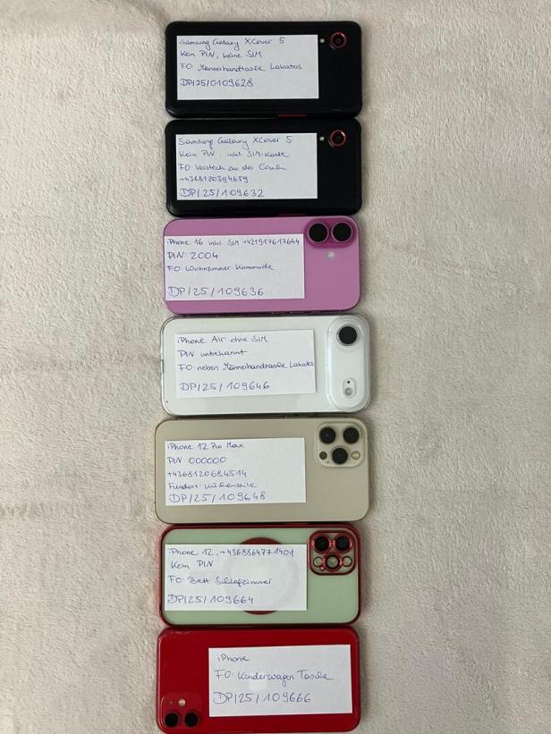 Sieben Smartphones liegen nebeneinander, auf jedem liegt ein Zettel mit handschriftlichen Notizen zu Gerätedaten und Fundort.