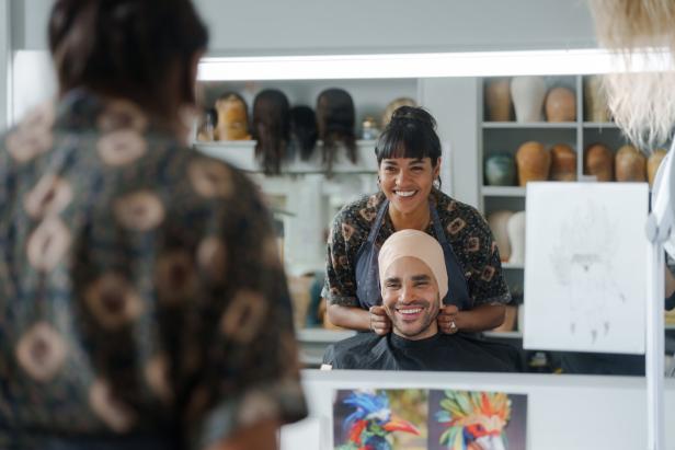 Szenenfoto: Maya (Salka Weber) bereitet die Maske für Tänzer Philip (Patrick Isermeyer) vor, beide sind vor einem Spiegel und lachen.
