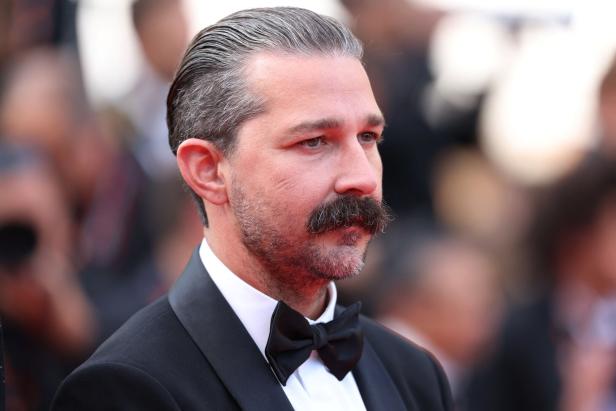 Shia LaBeouf mit zurückgekämmtem Haar und Schnurrbart trägt einen Smoking mit Fliege.