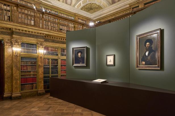 Gemälde und Zeichnung in edlem Ausstellungsraum mit historischen Bücherregalen und Stuckdecke.