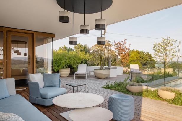 Moderne Terrasse mit Loungemöbeln, Holzdeck, Pflanzenkübeln und Blick auf Garten und Pool.