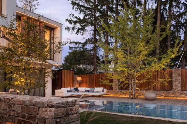 Modernes Haus mit Pool und Steinmauer im Garten, umgeben von grüner Landschaft.