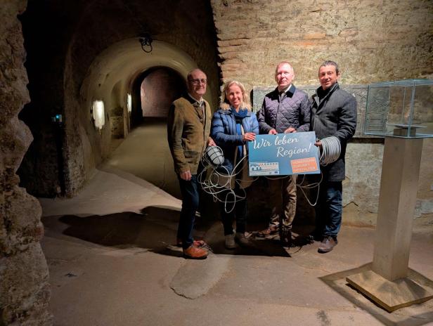 Vier Personen stehen in einem historischen Gewölbegang und halten ein Schild mit der Aufschrift „Wir leben Region!“.